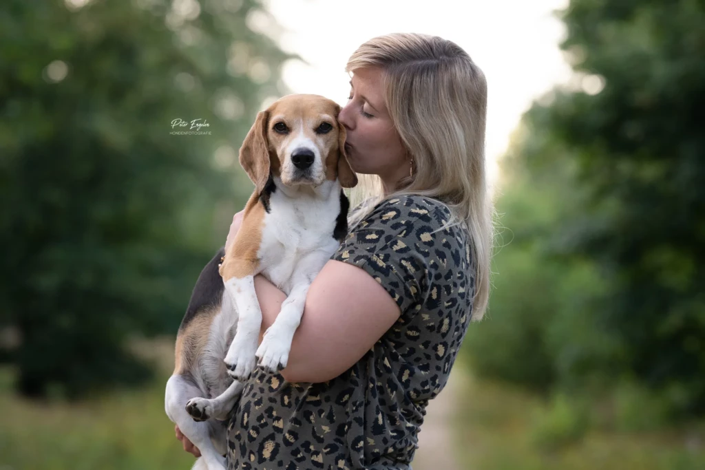 Een Beagle in de armen van haar baasje met als achtergrond een bos.
